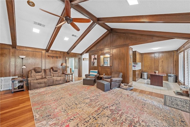 living room featuring vaulted ceiling with beams, wood walls, ceiling fan, and light hardwood / wood-style floors