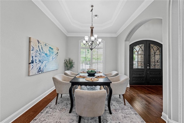 dining space featuring french doors, a raised ceiling, a notable chandelier, hardwood / wood-style flooring, and ornamental molding