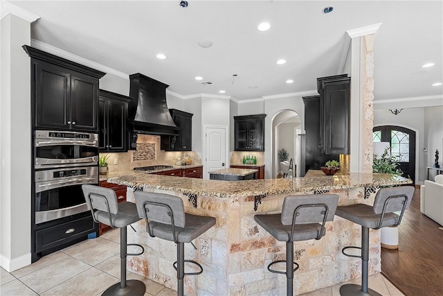 kitchen featuring a kitchen breakfast bar, custom exhaust hood, light tile patterned floors, kitchen peninsula, and stainless steel appliances