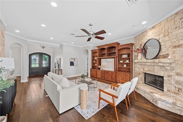 living room with french doors, a stone fireplace, crown molding, dark hardwood / wood-style floors, and ceiling fan