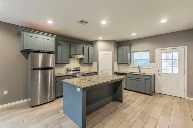 kitchen with sink, light hardwood / wood-style floors, a kitchen island, light stone counters, and stainless steel appliances