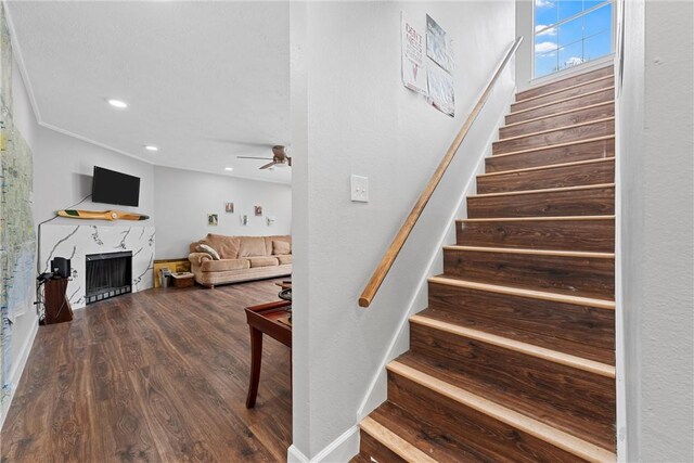 stairs featuring wood-type flooring, ceiling fan, and a fireplace