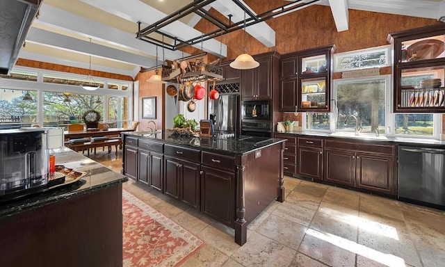 kitchen with dark stone counters, vaulted ceiling with beams, a kitchen island with sink, stone tile flooring, and black appliances