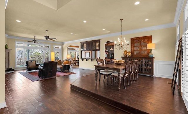 dining space featuring ceiling fan with notable chandelier, dark wood finished floors, arched walkways, wainscoting, and crown molding