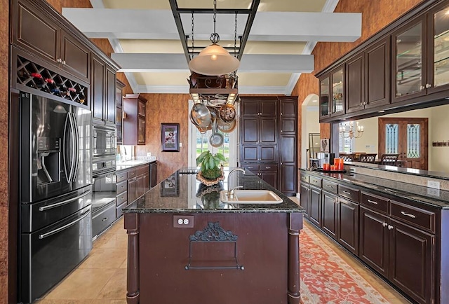 kitchen with dark stone counters, a kitchen island with sink, a sink, black appliances, and glass insert cabinets