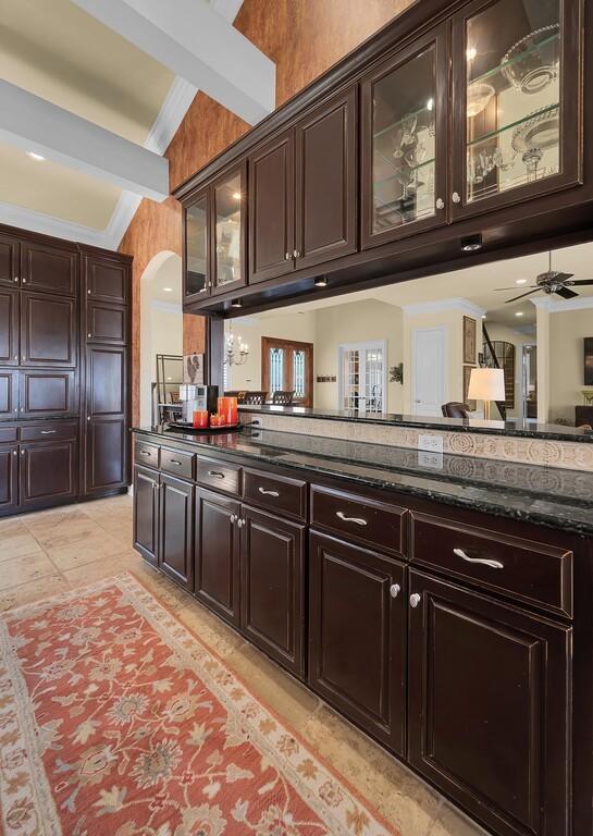 kitchen featuring arched walkways, dark brown cabinetry, dark stone countertops, and crown molding