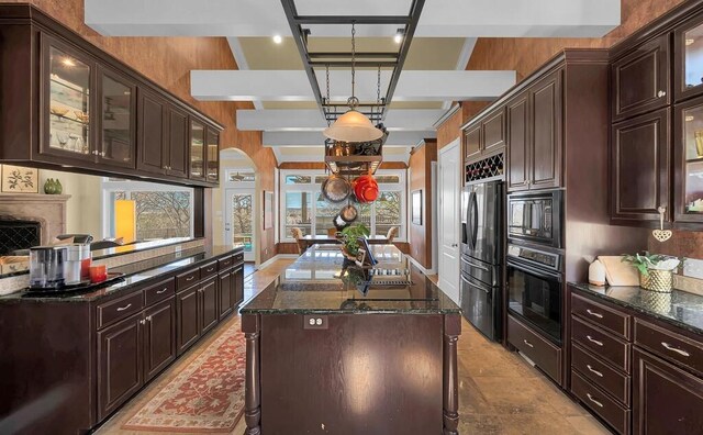 kitchen with dark stone countertops, arched walkways, black appliances, dark brown cabinets, and a center island