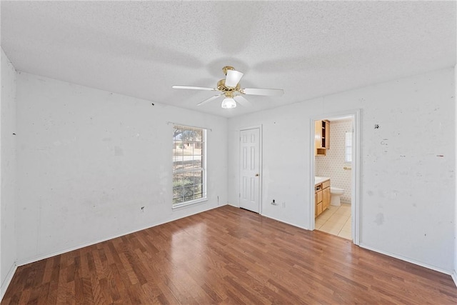 unfurnished bedroom with a closet, light wood-style flooring, a textured ceiling, and ensuite bathroom