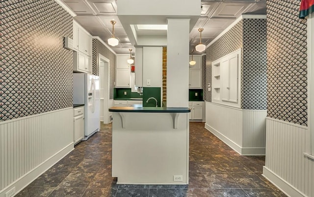 kitchen featuring a breakfast bar, white cabinets, sink, white fridge with ice dispenser, and decorative light fixtures