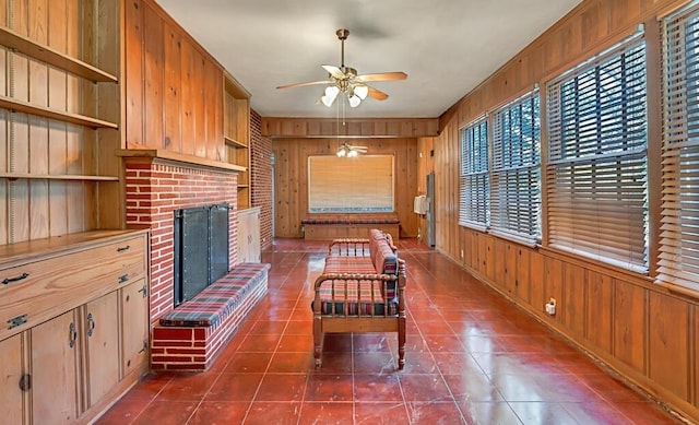 unfurnished living room featuring plenty of natural light, wood walls, a fireplace, and ceiling fan