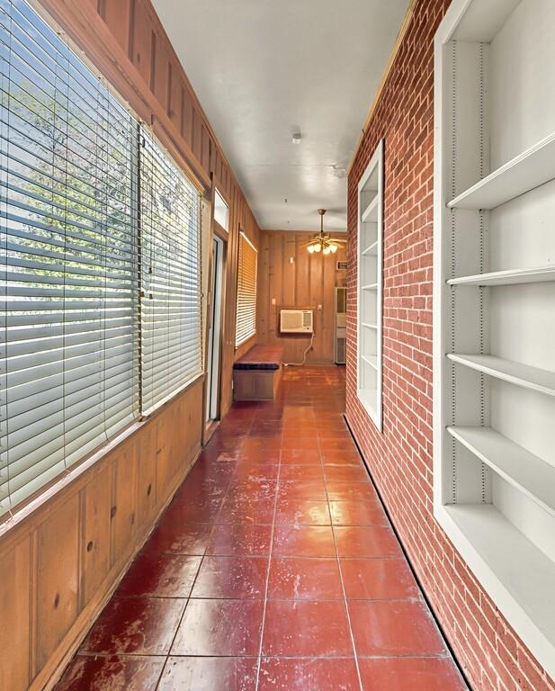 hallway featuring tile patterned flooring, a wall mounted AC, brick wall, and a chandelier