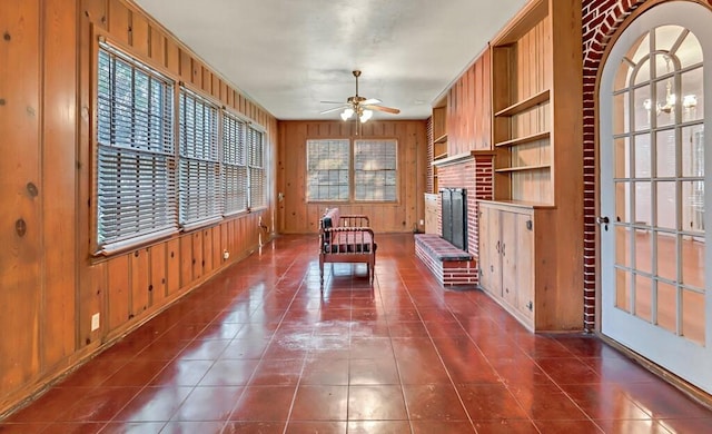 unfurnished dining area with a fireplace, plenty of natural light, wooden walls, and ceiling fan