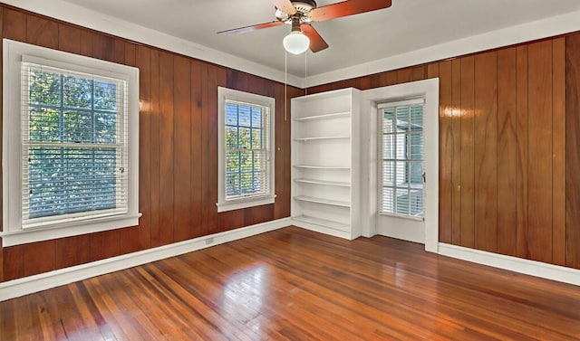 unfurnished room featuring a wealth of natural light, dark hardwood / wood-style flooring, ceiling fan, and wooden walls