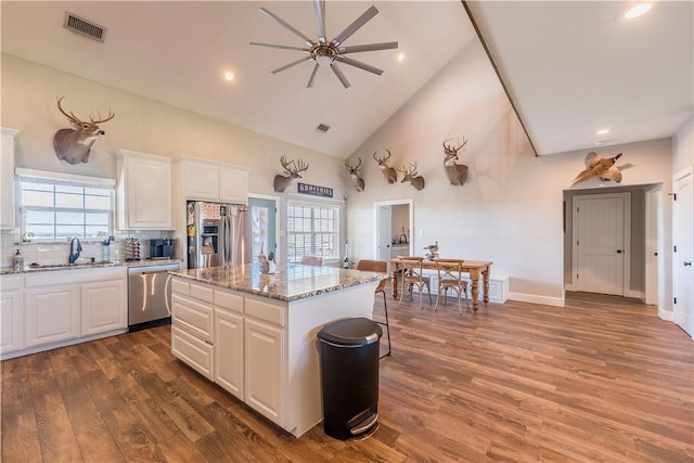 kitchen featuring light stone countertops, appliances with stainless steel finishes, dark wood-type flooring, a center island, and white cabinetry