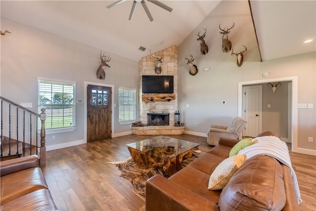 living room with a stone fireplace, ceiling fan, high vaulted ceiling, and hardwood / wood-style flooring