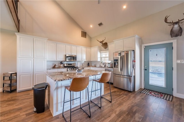 kitchen featuring light stone countertops, stainless steel appliances, a kitchen island, high vaulted ceiling, and white cabinets