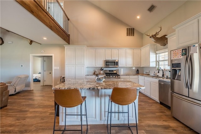 kitchen with high vaulted ceiling, a kitchen island, white cabinetry, and appliances with stainless steel finishes