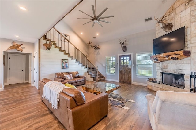 living room featuring hardwood / wood-style flooring, ceiling fan, a stone fireplace, and high vaulted ceiling