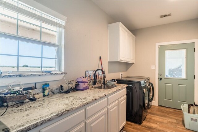 clothes washing area featuring washer and dryer, light hardwood / wood-style floors, cabinets, and sink