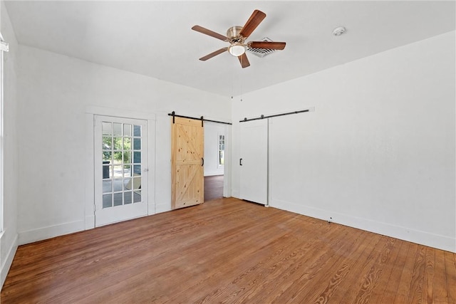 empty room with hardwood / wood-style floors, ceiling fan, and a barn door