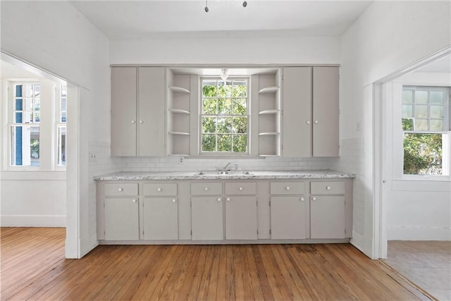 kitchen with sink, decorative backsplash, gray cabinets, light stone countertops, and light wood-type flooring