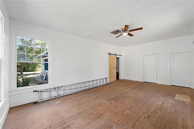 empty room featuring ceiling fan, a barn door, and wood-type flooring