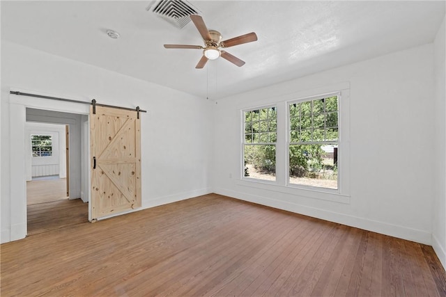 empty room featuring light wood-type flooring, a barn door, and ceiling fan