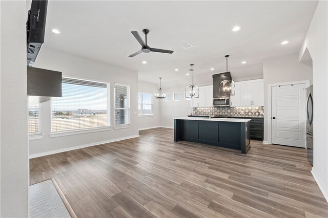 kitchen with light wood finished floors, decorative backsplash, open floor plan, stainless steel appliances, and white cabinetry