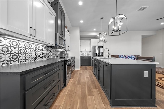 kitchen with an island with sink, light wood-style flooring, appliances with stainless steel finishes, white cabinetry, and a sink