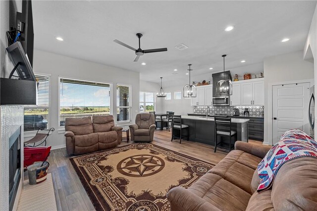 living area with a fireplace with flush hearth, recessed lighting, visible vents, and light wood finished floors