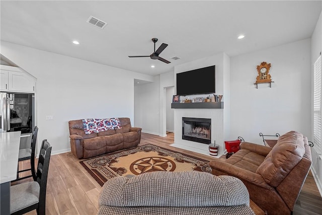 living room with light wood-type flooring, a fireplace with flush hearth, visible vents, and recessed lighting