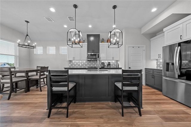 kitchen featuring stainless steel appliances, visible vents, backsplash, and light wood finished floors