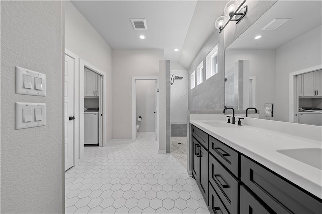 bathroom featuring a tile shower, washer / dryer, a sink, and visible vents