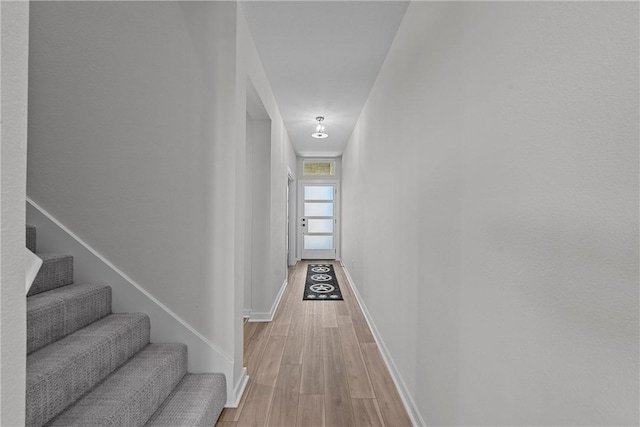 hall featuring light wood-style flooring, stairway, and baseboards