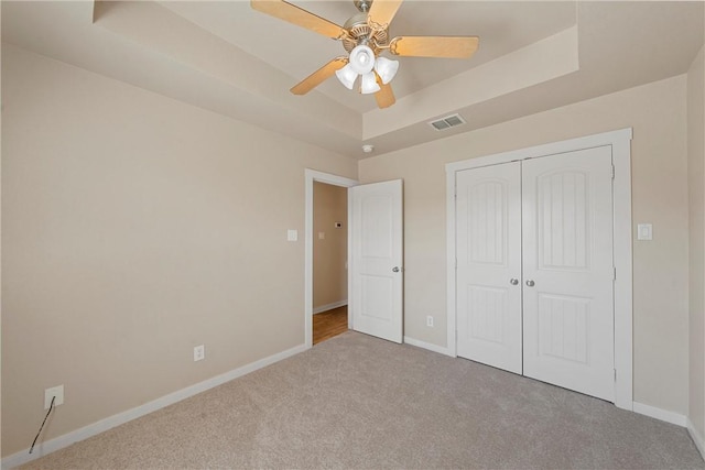 unfurnished bedroom featuring light carpet, a closet, a raised ceiling, and ceiling fan