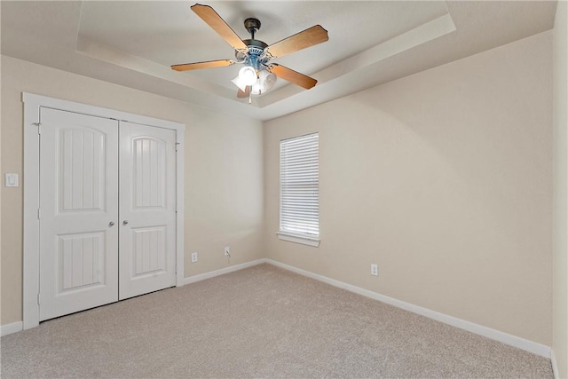 unfurnished bedroom with ceiling fan, a closet, light carpet, and a tray ceiling