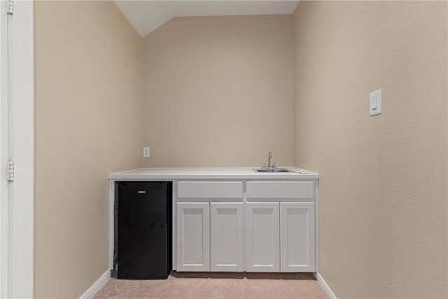 bar with black fridge, light colored carpet, sink, white cabinetry, and lofted ceiling