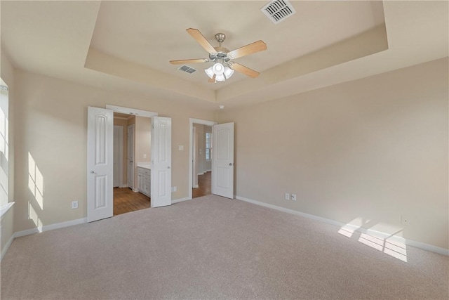 unfurnished bedroom featuring a tray ceiling, ceiling fan, and light carpet