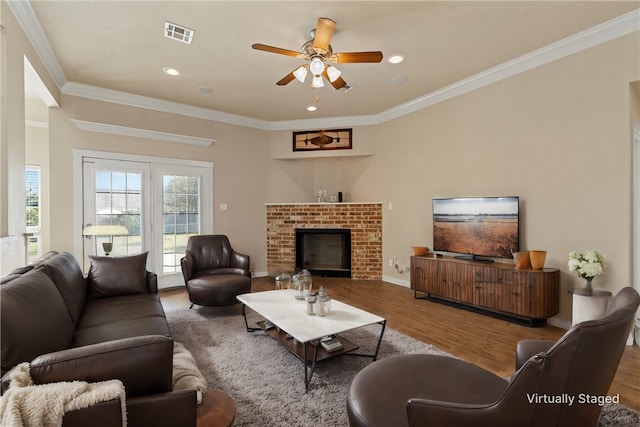 living room with hardwood / wood-style floors, a brick fireplace, ceiling fan, and ornamental molding