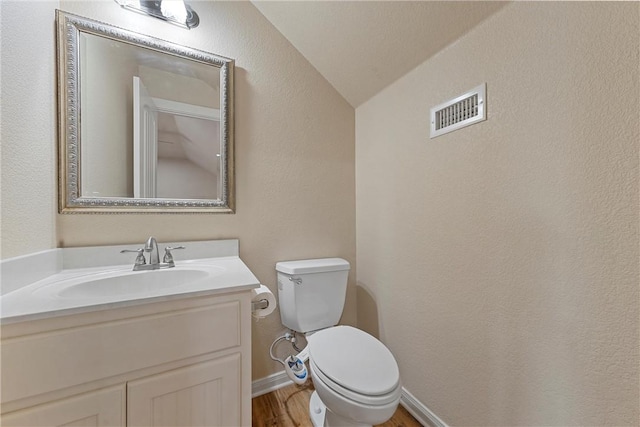 bathroom featuring toilet, vanity, hardwood / wood-style flooring, and vaulted ceiling