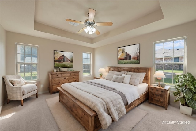 bedroom with a raised ceiling, multiple windows, ceiling fan, and light colored carpet