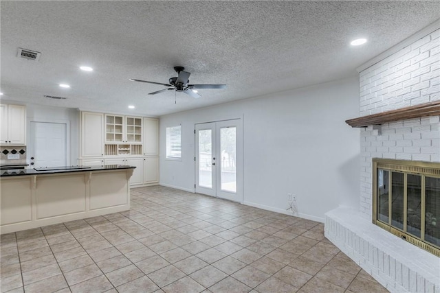 unfurnished living room with french doors, light tile patterned floors, a textured ceiling, and a brick fireplace