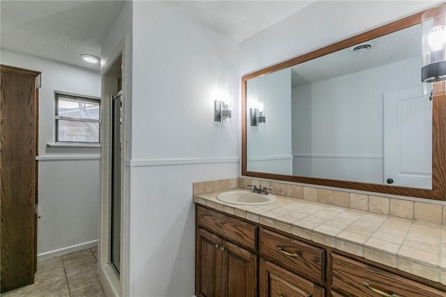 bathroom featuring tile patterned flooring, vanity, a textured ceiling, and a shower with door