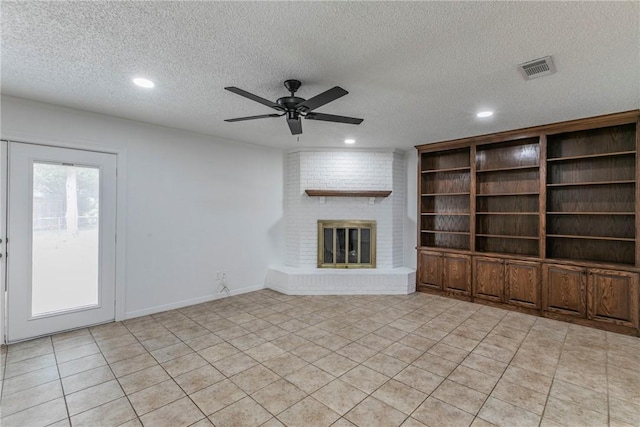 unfurnished living room featuring ceiling fan, light tile patterned floors, a textured ceiling, and a brick fireplace