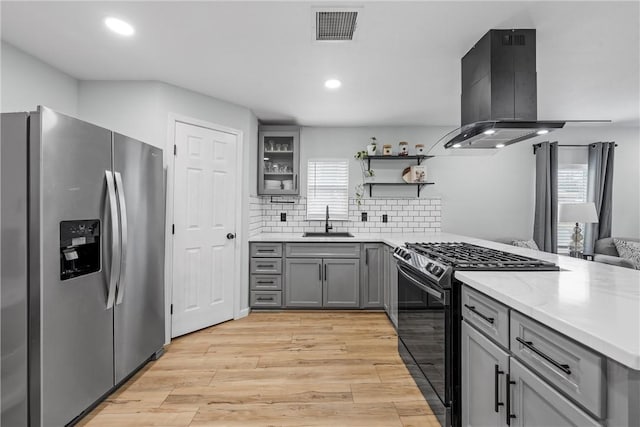 kitchen featuring island exhaust hood, black gas range oven, gray cabinetry, a sink, and stainless steel fridge