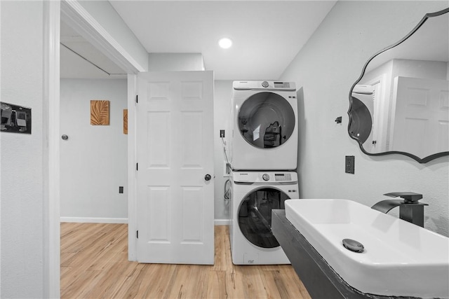 clothes washing area with stacked washer and dryer, light wood-type flooring, a sink, and laundry area