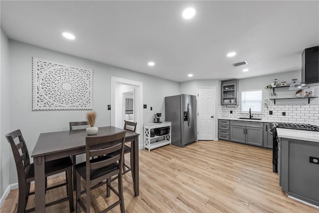 kitchen with a sink, visible vents, appliances with stainless steel finishes, light wood-type flooring, and backsplash