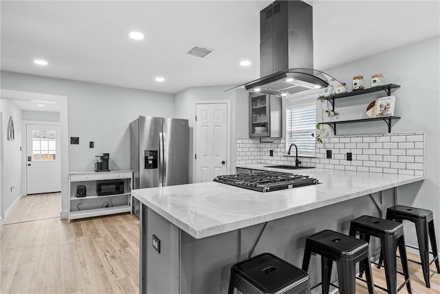 kitchen featuring island exhaust hood, gas stovetop, visible vents, stainless steel fridge, and a peninsula