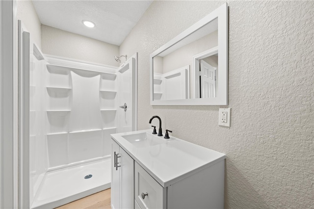 bathroom with a textured ceiling, vanity, and walk in shower