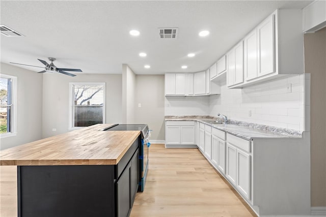 kitchen featuring wooden counters, black range with electric stovetop, sink, a kitchen island, and white cabinetry